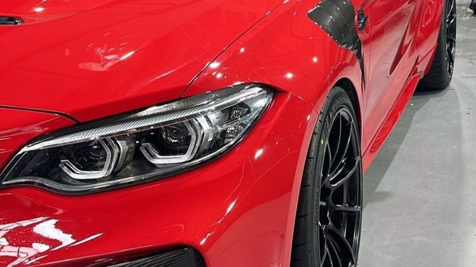 Automóvil rojo deportivo con detalles en fibra de carbono en la carrocería, especialmente en el guardabarros y alrededor de los faros delanteros. Las llantas negras son de perfil bajo y diseño deportivo.